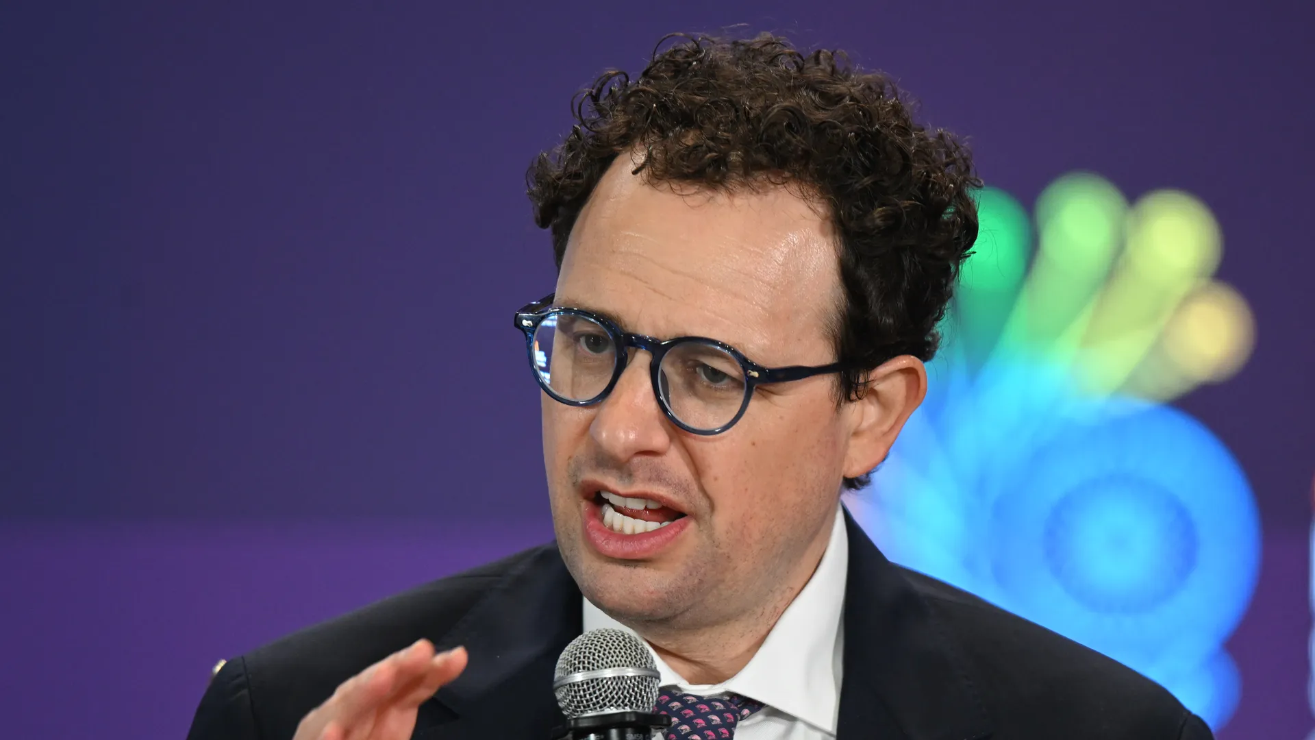 Anthropic CEO Dario Amodei speaking into a microphone on a CNBC stage in front of the NBC peacock backdrop, the cable-news setting where the 'white collar bloodbath' framing has been delivered to the broadest audience.